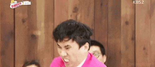 a man in a pink shirt is making a funny face while sitting in front of a wooden wall .