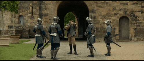 a group of men in armor are standing in front of a stone building
