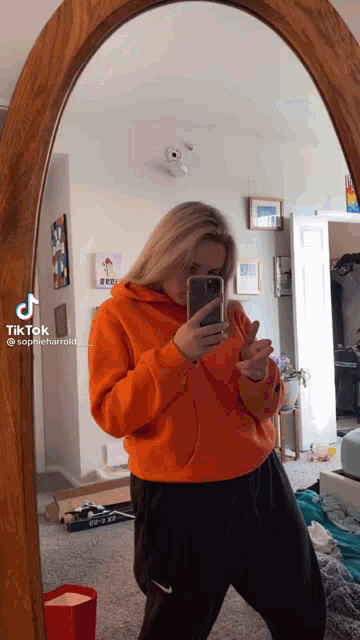 a woman in an orange hoodie is taking a selfie in front of a mirror with the hashtag tiktok