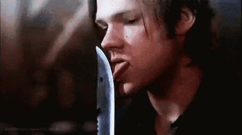 a close up of a man licking a knife with his tongue out .