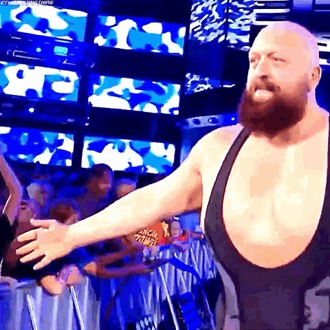 a bearded wrestler in a black singlet is standing in front of a crowd .