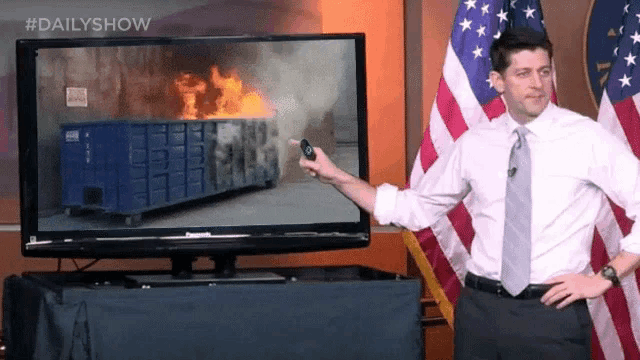 a man stands in front of an american flag while pointing at a dumpster on a television screen that says dailyshow