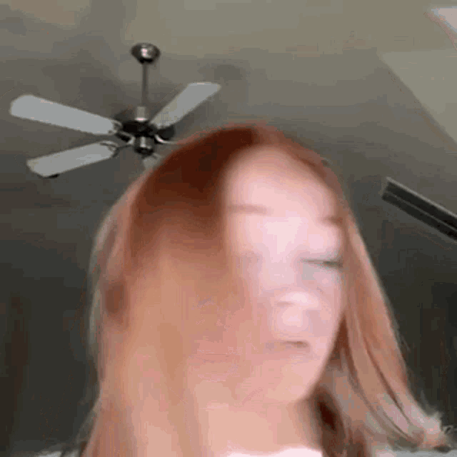 a woman with red hair is standing in front of a ceiling fan and making a funny face .