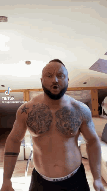 a shirtless man with a tattoo on his chest is standing in a living room