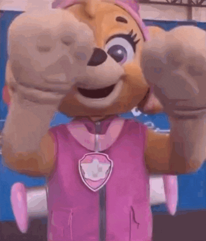a mascot from paw patrol is wearing a pink vest and a pink headband .