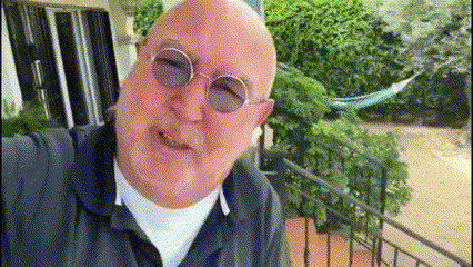a bald man wearing sunglasses and a blue shirt is taking a selfie on a balcony .