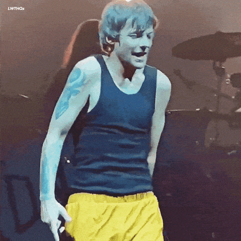 a man in a blue tank top and yellow shorts stands on stage