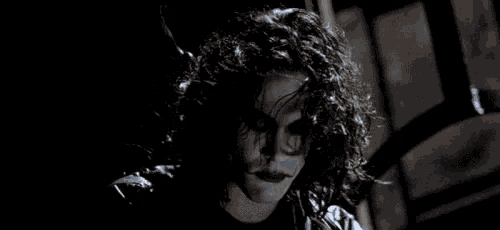 a close up of a person with curly hair in a dark room with a black jacket on .