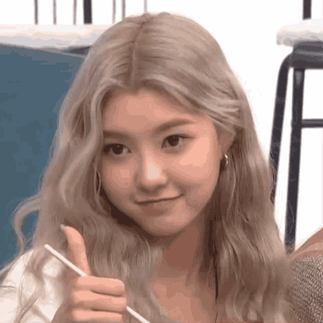 a woman with blonde hair is holding a chopstick and giving a thumbs up .