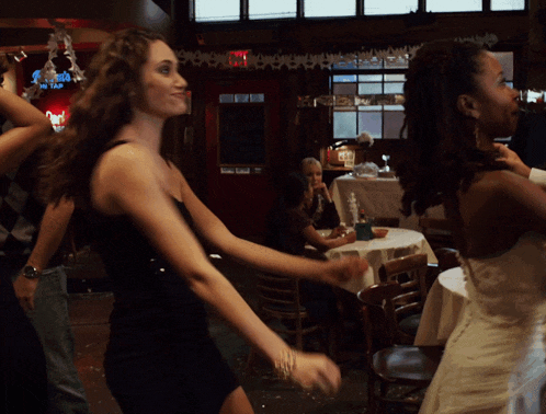 a woman in a black dress is dancing in a room with a sign that says ' angels on tap '