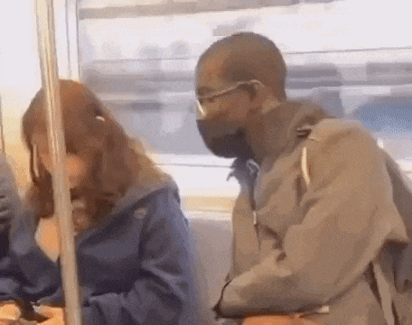 a man wearing a mask and glasses is sitting next to a woman on a train .