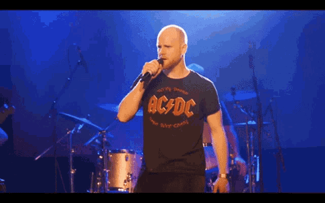 a man singing into a microphone wearing a black ac dc t-shirt