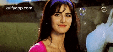 a woman wearing a purple headband and a pink top is smiling .