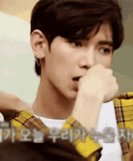 a close up of a young man wearing a yellow plaid shirt covering his mouth with his hand .