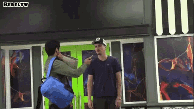 a man pointing at another man in front of a building that says rebeltv on it