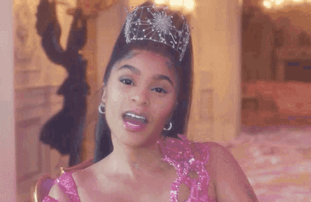 a woman wearing a pink dress and a tiara is sitting on a chair .
