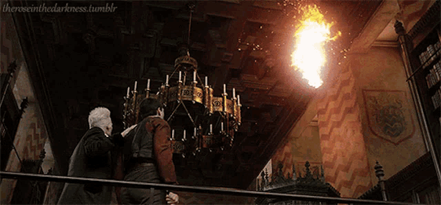 two men are standing in front of a chandelier with a fire coming out of it ..
