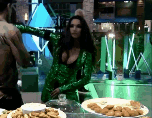 a woman in a green sequined dress is standing in front of a display of food