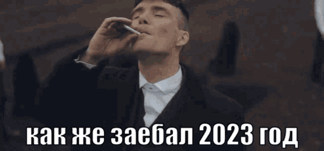 a man in a suit and tie is smoking a cigarette with the words " как же заебал 2023 год " above him