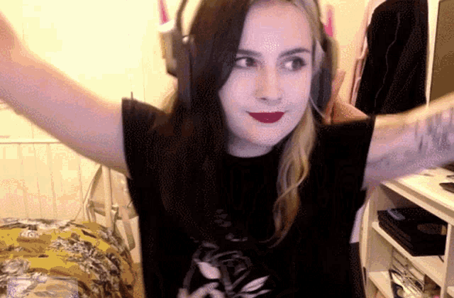 a woman wearing headphones has her arms outstretched and looks at the camera
