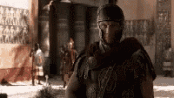 a man in a helmet and armor is standing in a room with other soldiers .