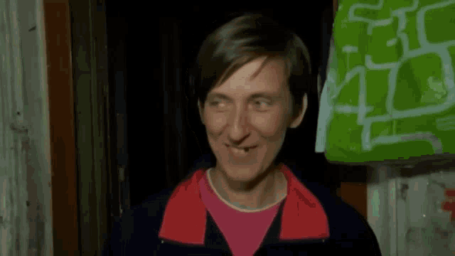 a woman with missing teeth is smiling in front of a green bag with graffiti on it .