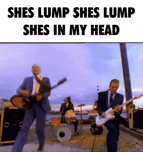 a man in a suit is playing a guitar in front of a drum set while another man is playing drums