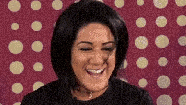 a woman in a black shirt is smiling in front of a pink background with white polka dots