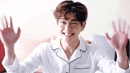 a young man wearing glasses and pajamas is sitting on a bed .