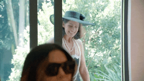 a woman wearing a hat and sunglasses is smiling