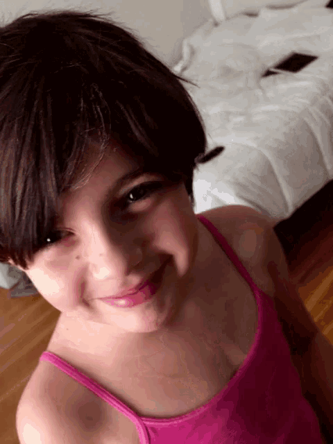 a little girl wearing a pink tank top is smiling