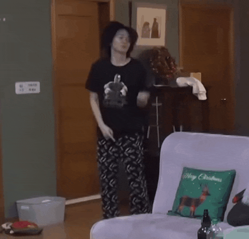 a woman is dancing in a living room with a couch and a pillow that says merry christmas .