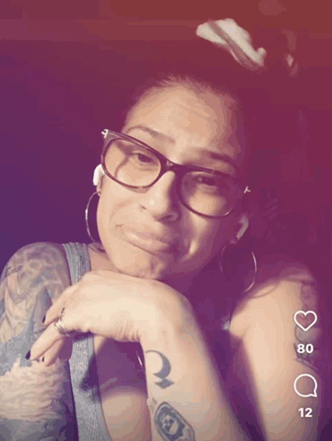 a woman wearing glasses and earrings has a tattoo on her arm that says " a "