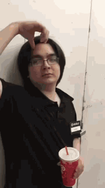 a man with glasses is holding a cup of soda and pointing at his forehead .