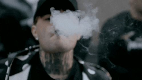 a man with a tattoo on his neck is blowing smoke from his mouth