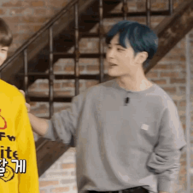 a man with blue hair is wearing a grey sweater and a yellow shirt
