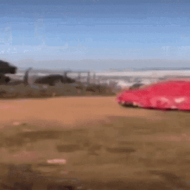 a red car is driving down a dirt road on a sunny day .