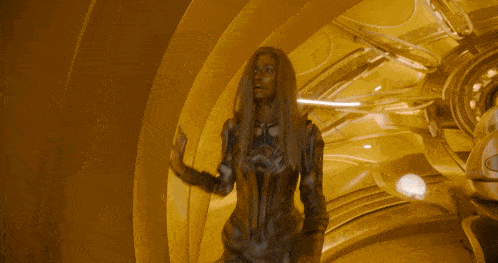 a woman with long blonde hair is standing in a room with a yellow wall