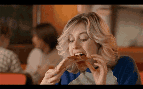 a woman is eating a slice of pizza with her mouth open