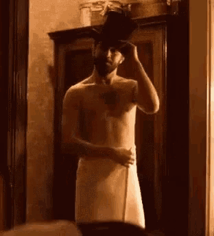 a shirtless man is wrapped in a towel and holding a hat .