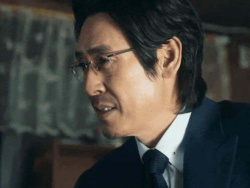a man wearing glasses and a suit looks to his left