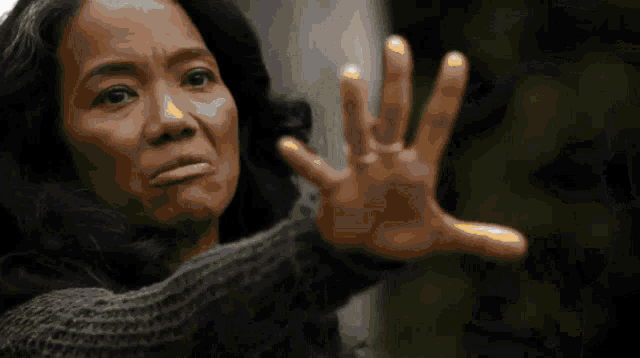 a woman in a grey sweater is making a face with her hand outstretched
