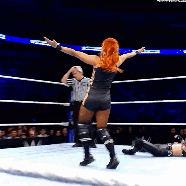 a woman in a wrestling ring with her arms outstretched and a referee behind her