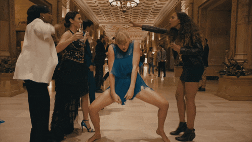 a woman in a blue dress is dancing with other women in a hallway