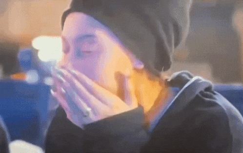 a woman is covering her mouth with her hands while wearing a black hat .
