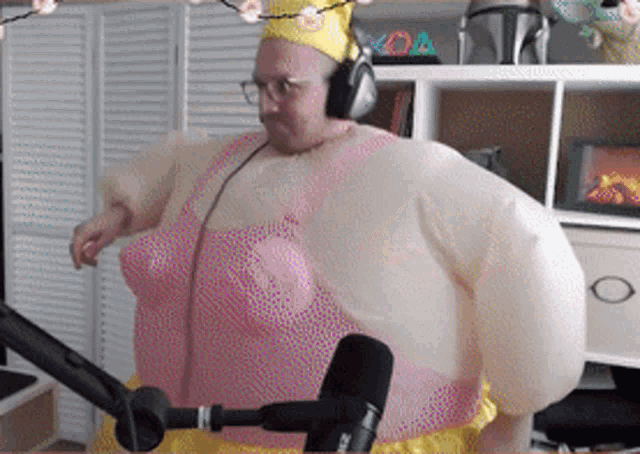 a man is wearing a pink dress and a crown while standing in front of a microphone .