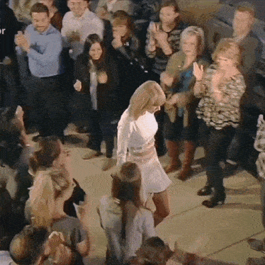 a woman in a white dress dancing in front of a crowd of people