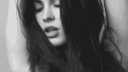 a black and white photo of a woman with her eyes closed and her hair blowing in the wind .