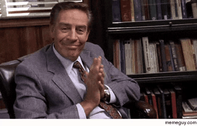 a man in a suit and tie is clapping his hands in front of a book shelf