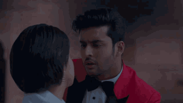 a man in a red suit and bow tie is kissing a woman on the cheek